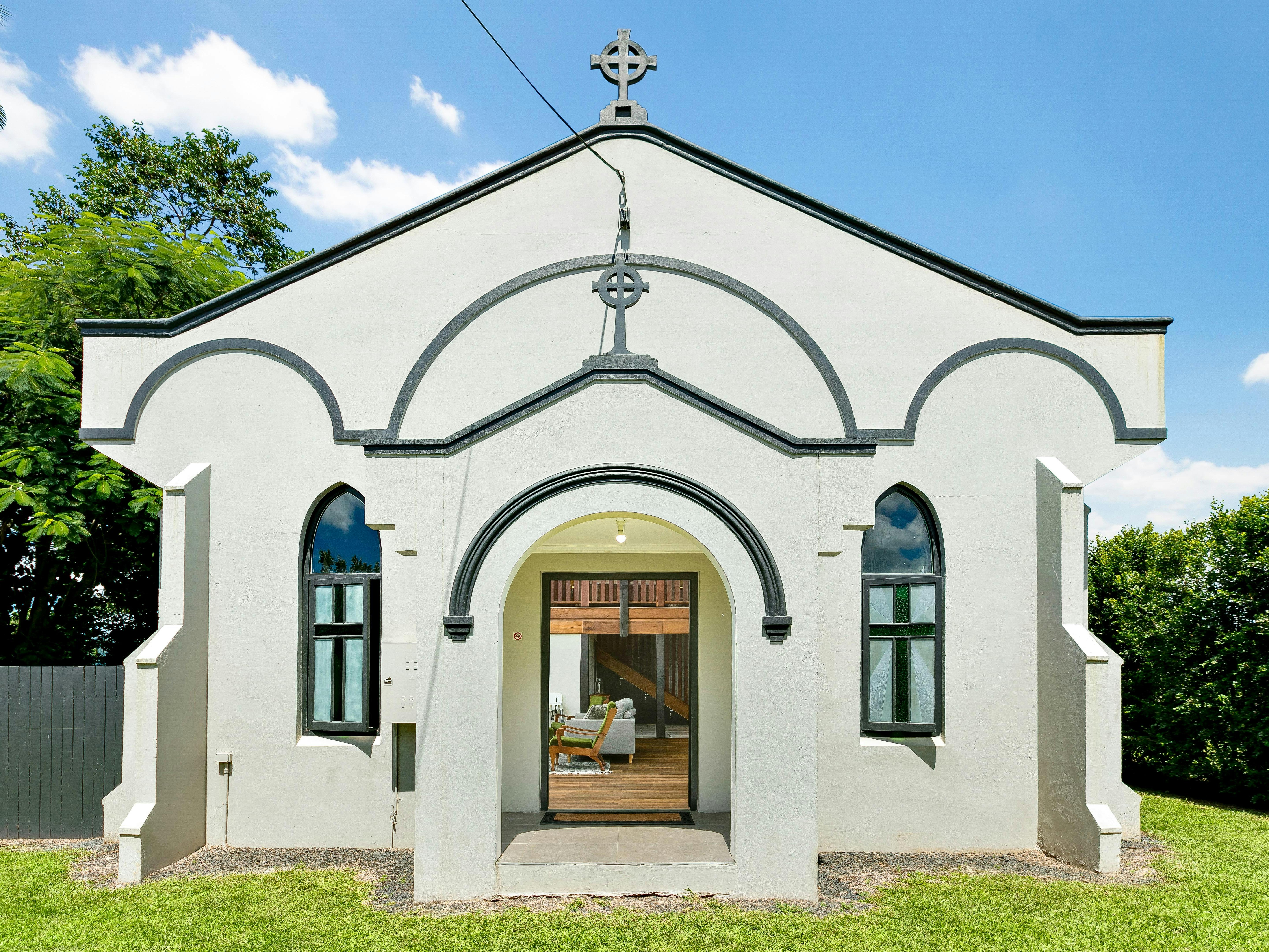 Shows the exterior of an old restored church on a sunny day. The church is white with black trim.